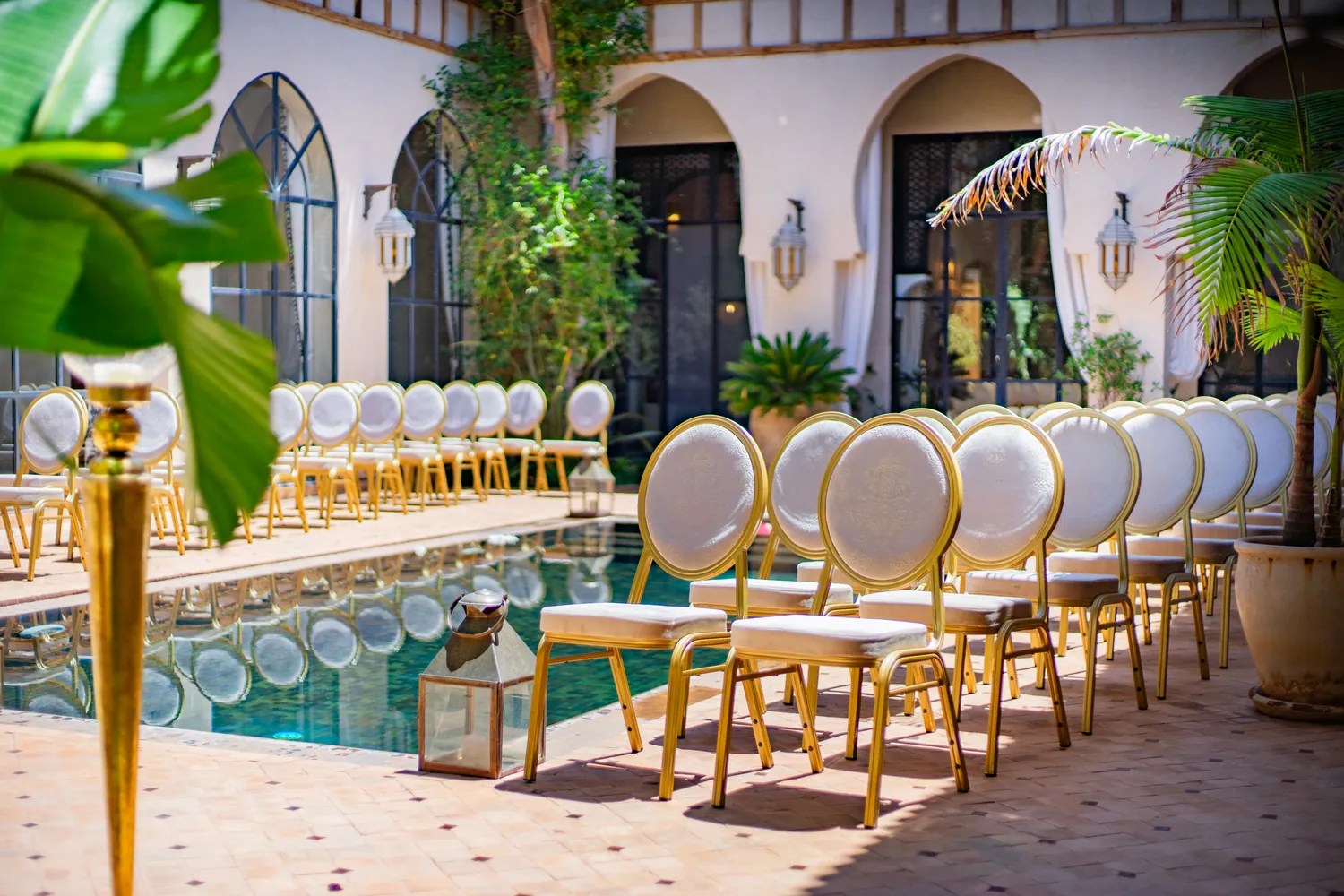 Gold ceremony chairs arranged around the reflecting pool at Daba Village, set for a wedding in the Marrakech sunshine