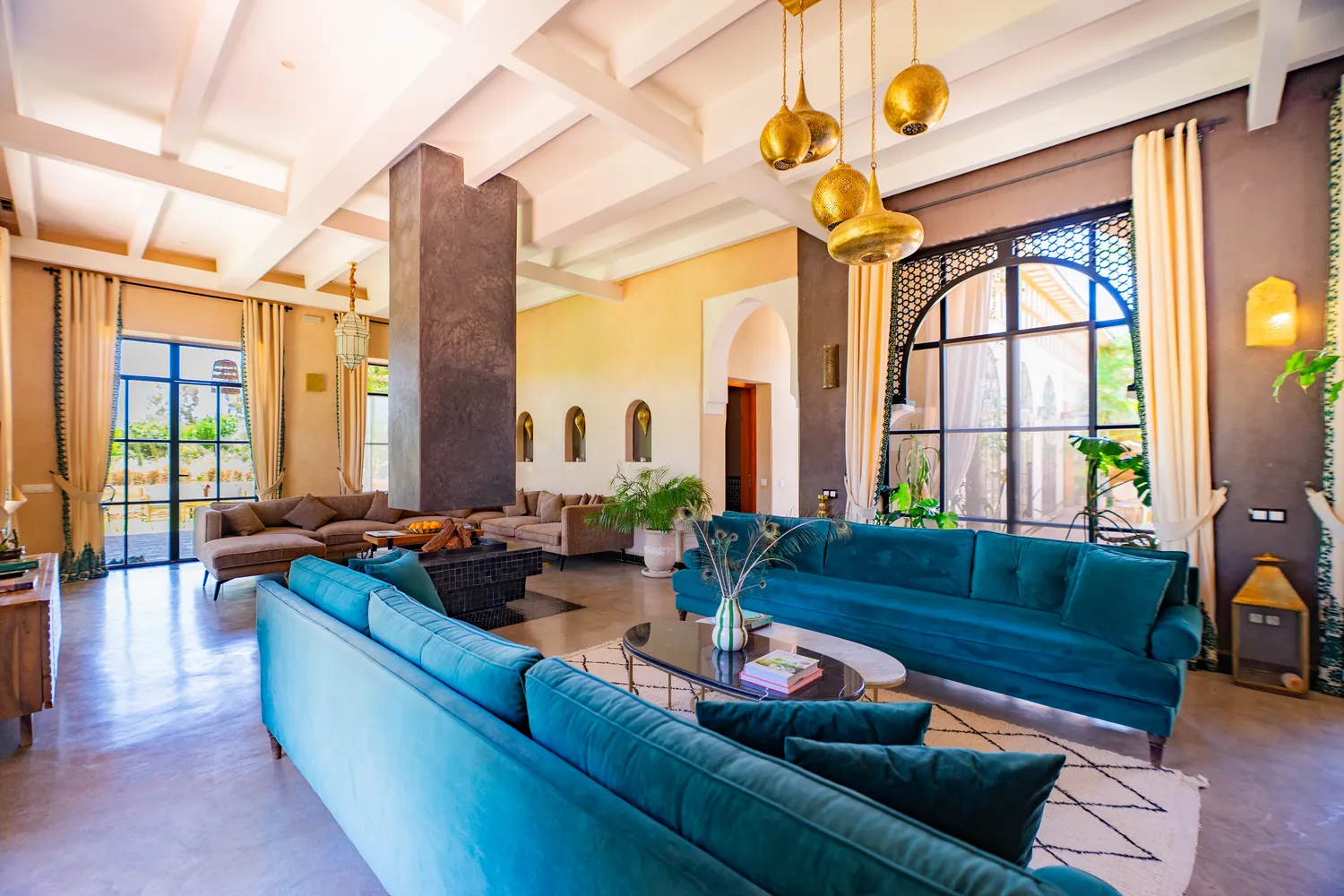 The spacious main salon at Daba Village with teal velvet sofas, brass Moroccan lanterns and tall arched windows